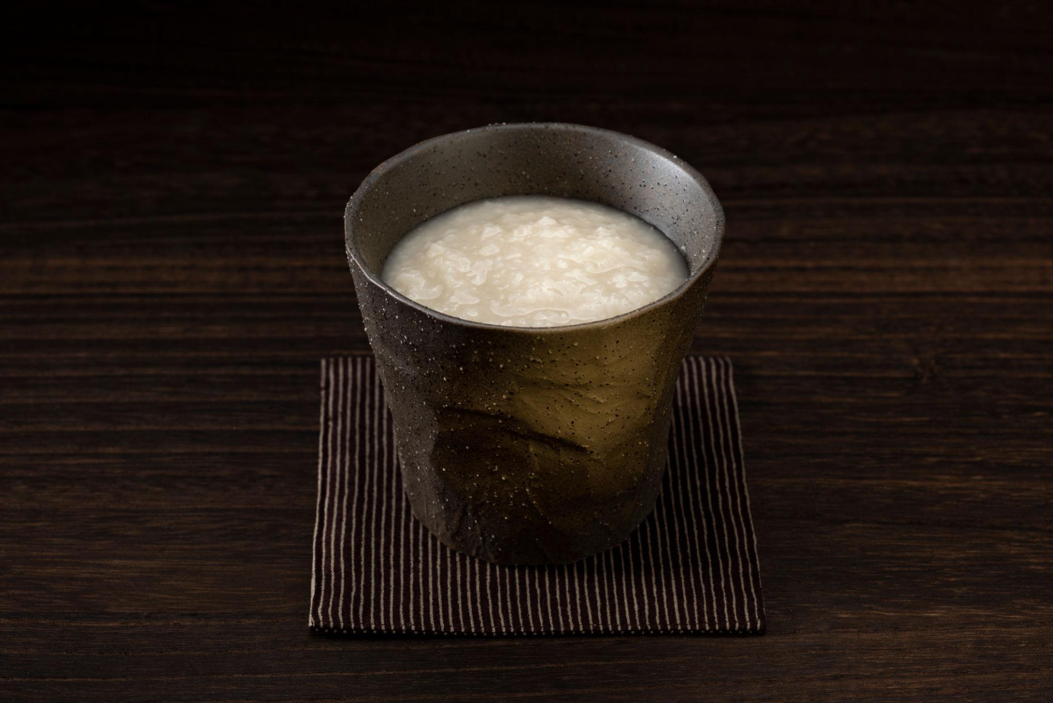 A ceramic cup of amazake on a dark wooden table